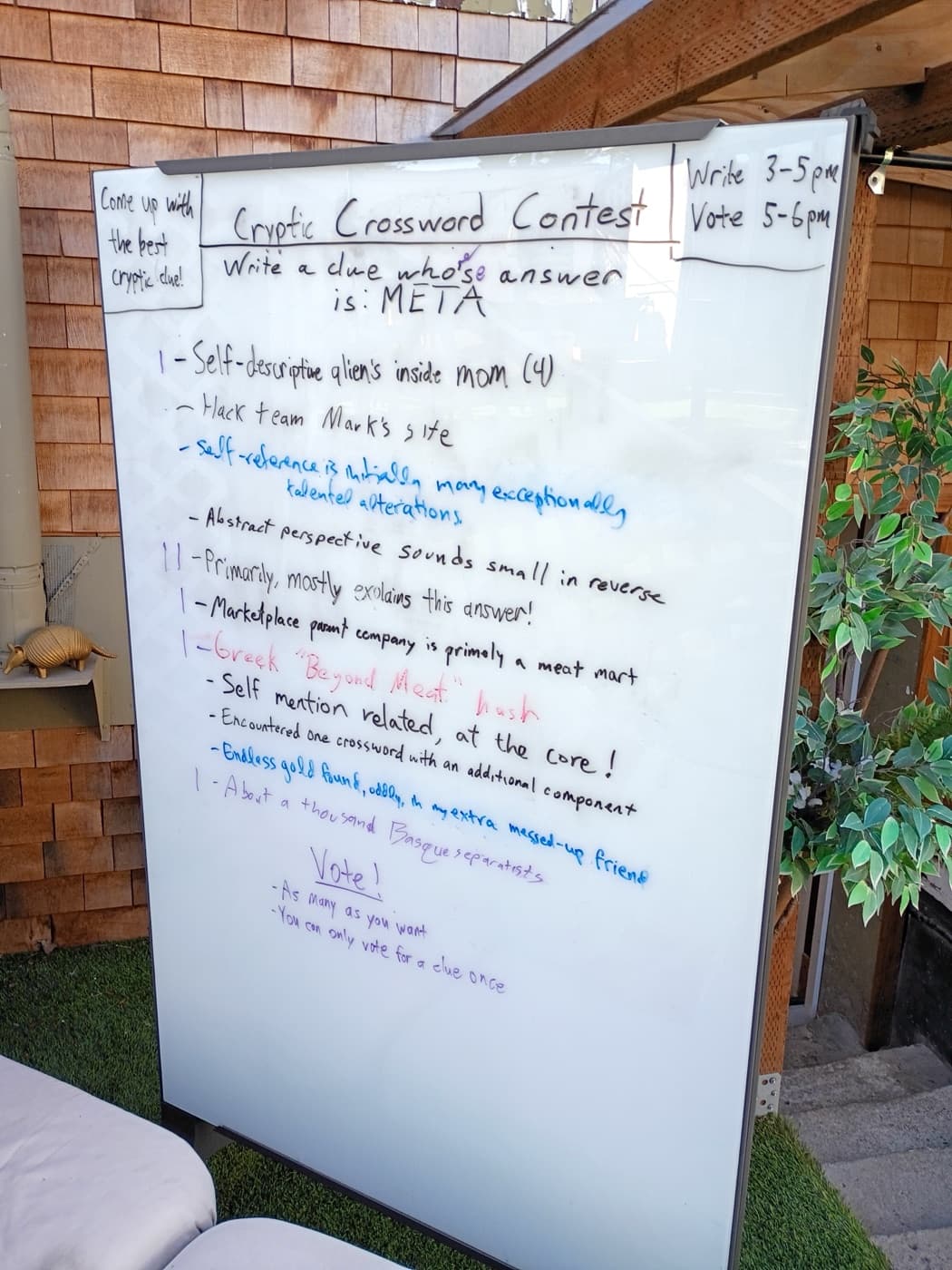 Whiteboard from the 2025 cryptic crossword contest, covered in handwritten clues whose answer is META